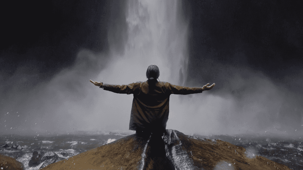 Traveler stands before powerful waterfall with arms raised, symbolizing adventure on the Sumatran Jungle River Expedition tour.