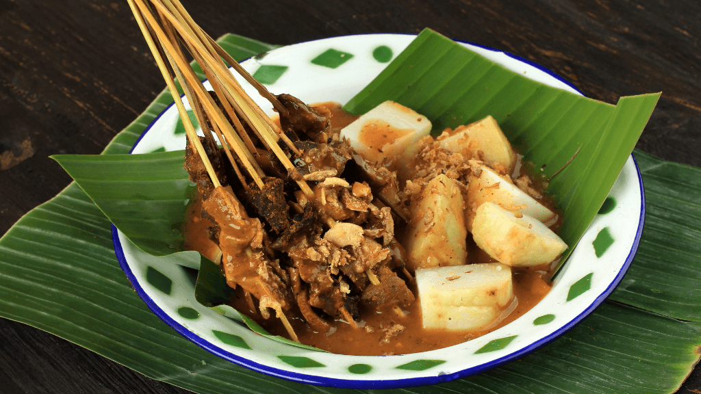Traditional Indonesian satay with rice cakes on banana leaf, part of the culinary experience on the Wild Orangutan 8-Day Loop.