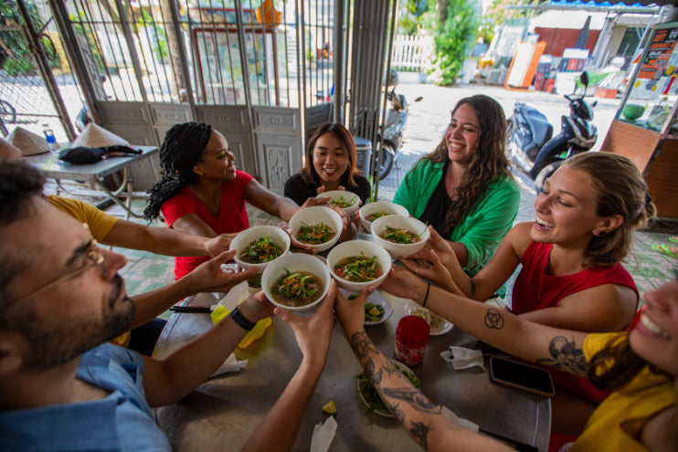 Group toasting with bowls of pho at a local Vietnamese eatery. Culinary bonding on Vietnam Hiking and Cycling Tour.