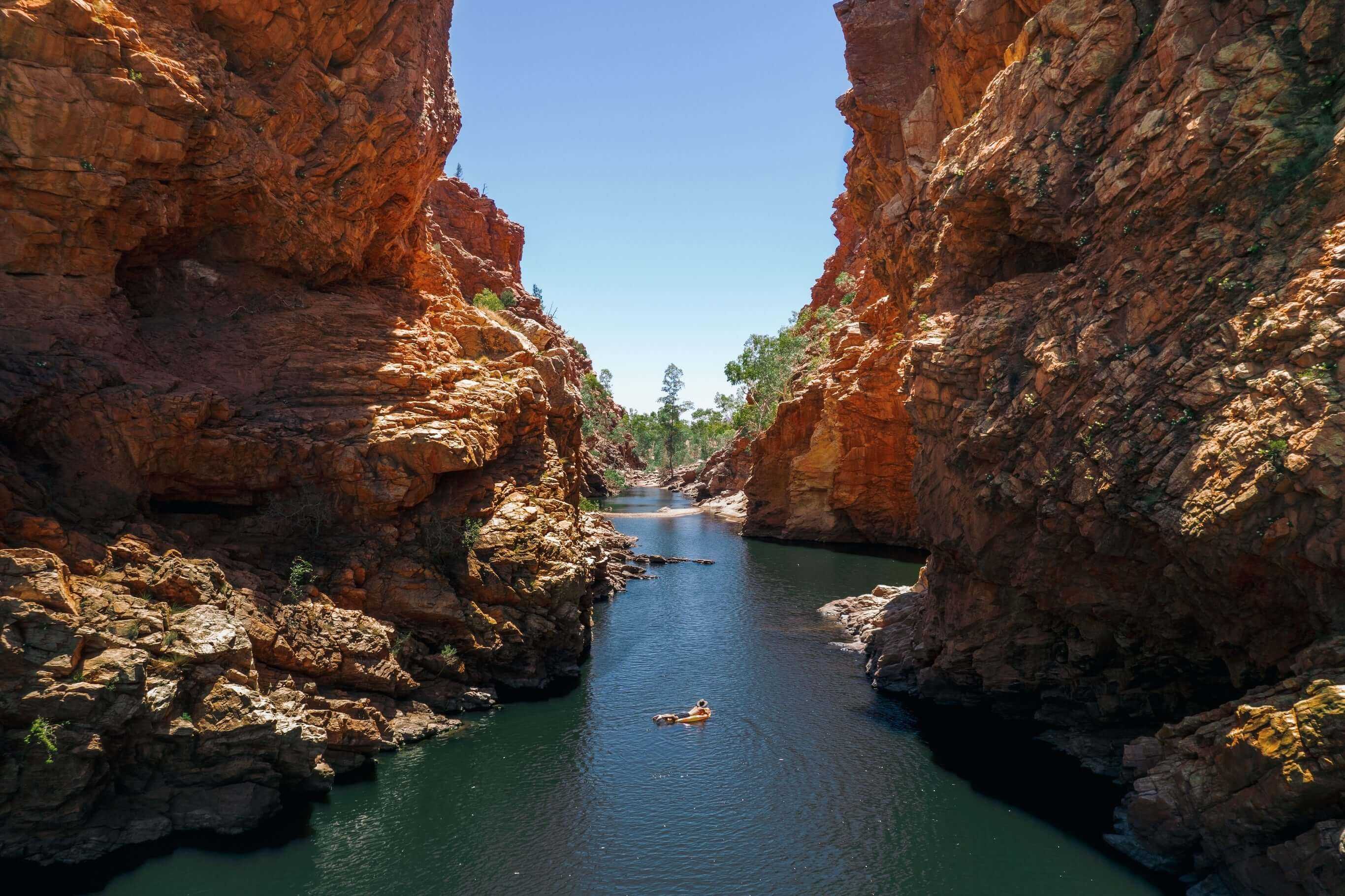 Person floating in narrow gorge waterway, a refreshing break during Larapinta Trail 5-Day Expedition in West MacDonnell Ranges.