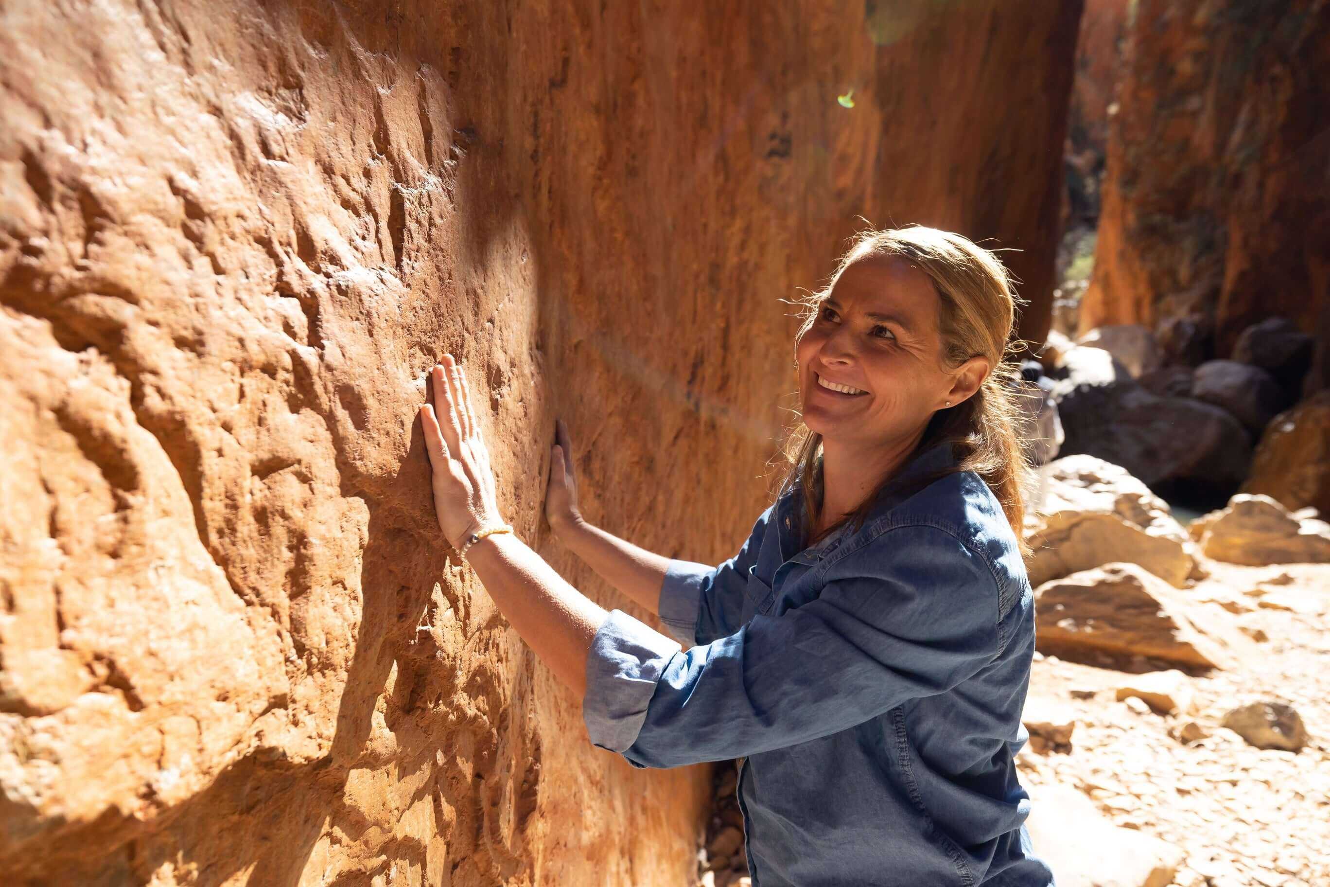 Woman touching ancient rock wall in Standley Chasm, a cultural highlight of the Larapinta Trail 5-Day Expedition experience.