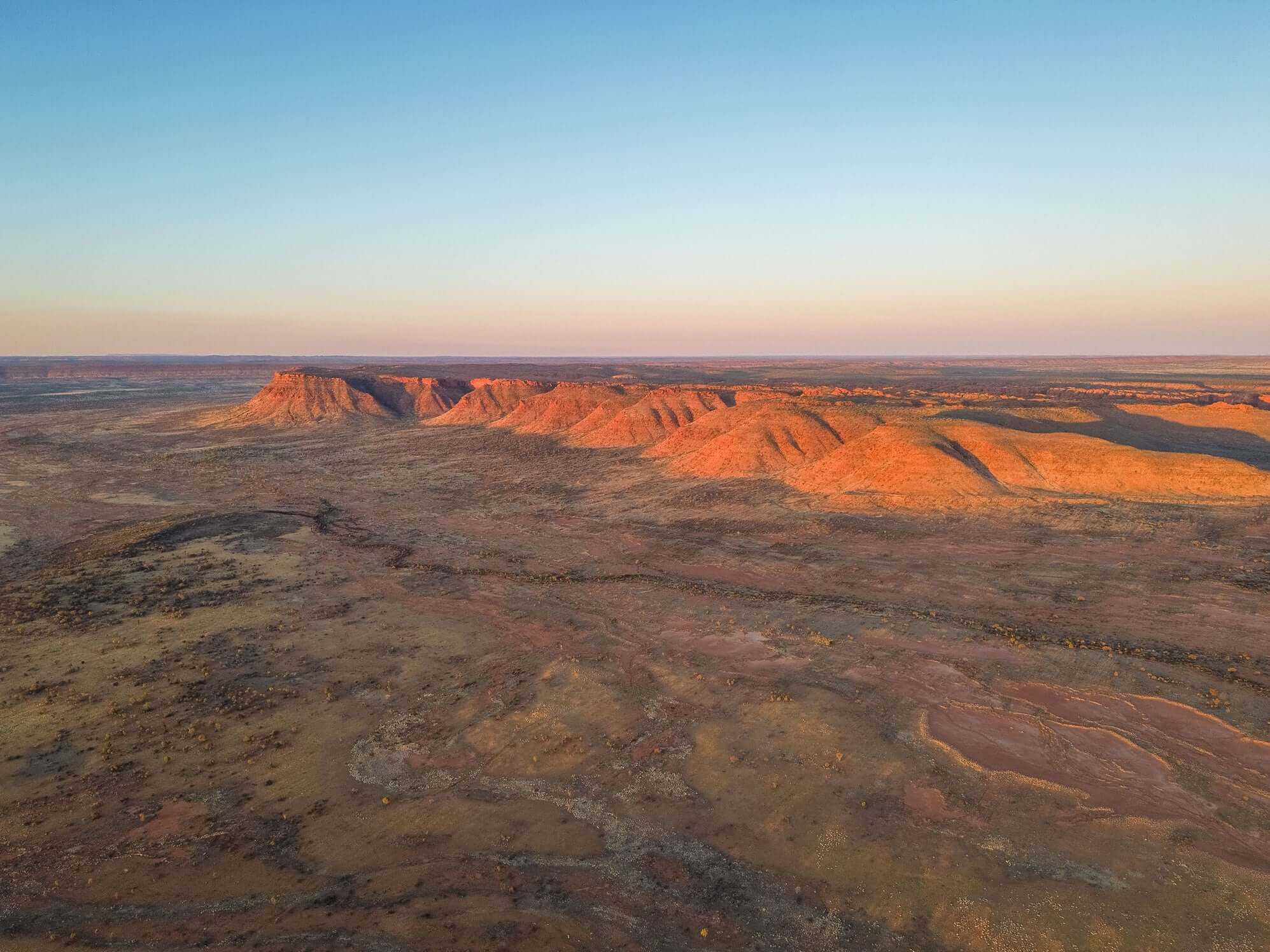 Aerial view of sunlit West MacDonnell Ranges, showcasing vast desert landscapes on Larapinta Trail 5-Day Expedition route.