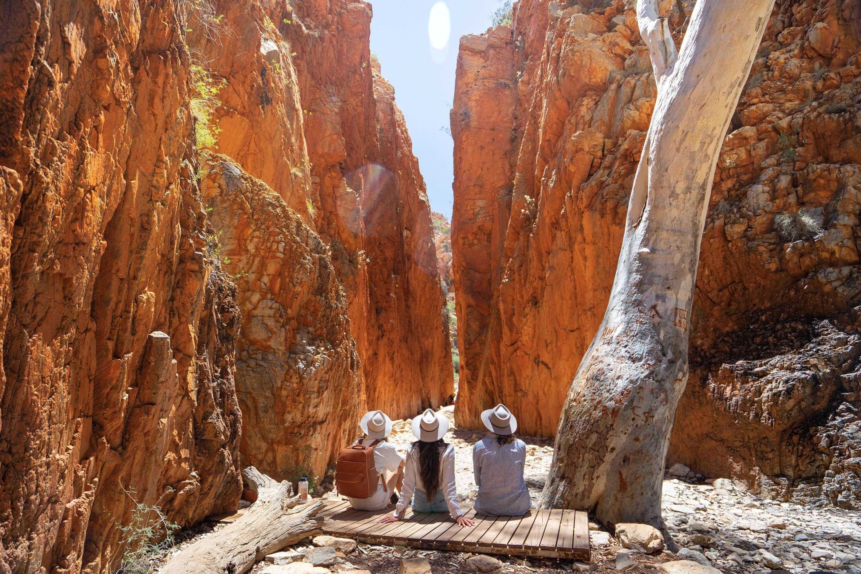 Travelers resting in a narrow gorge on the Uluru & Kings Canyon 4WD Safari, surrounded by towering red cliffs.