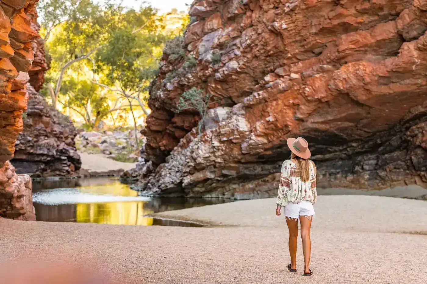 Woman exploring a serene gorge during the Uluru & Kings Canyon 4WD Safari, surrounded by red rock walls and tranquil water.