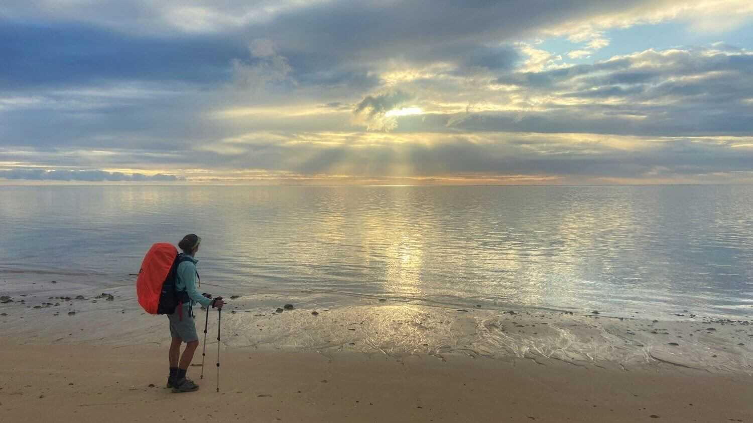 Hiker standing on beach at sunrise with trekking poles, enjoying the view during the 4-Day Ningaloo Kayak Expedition.