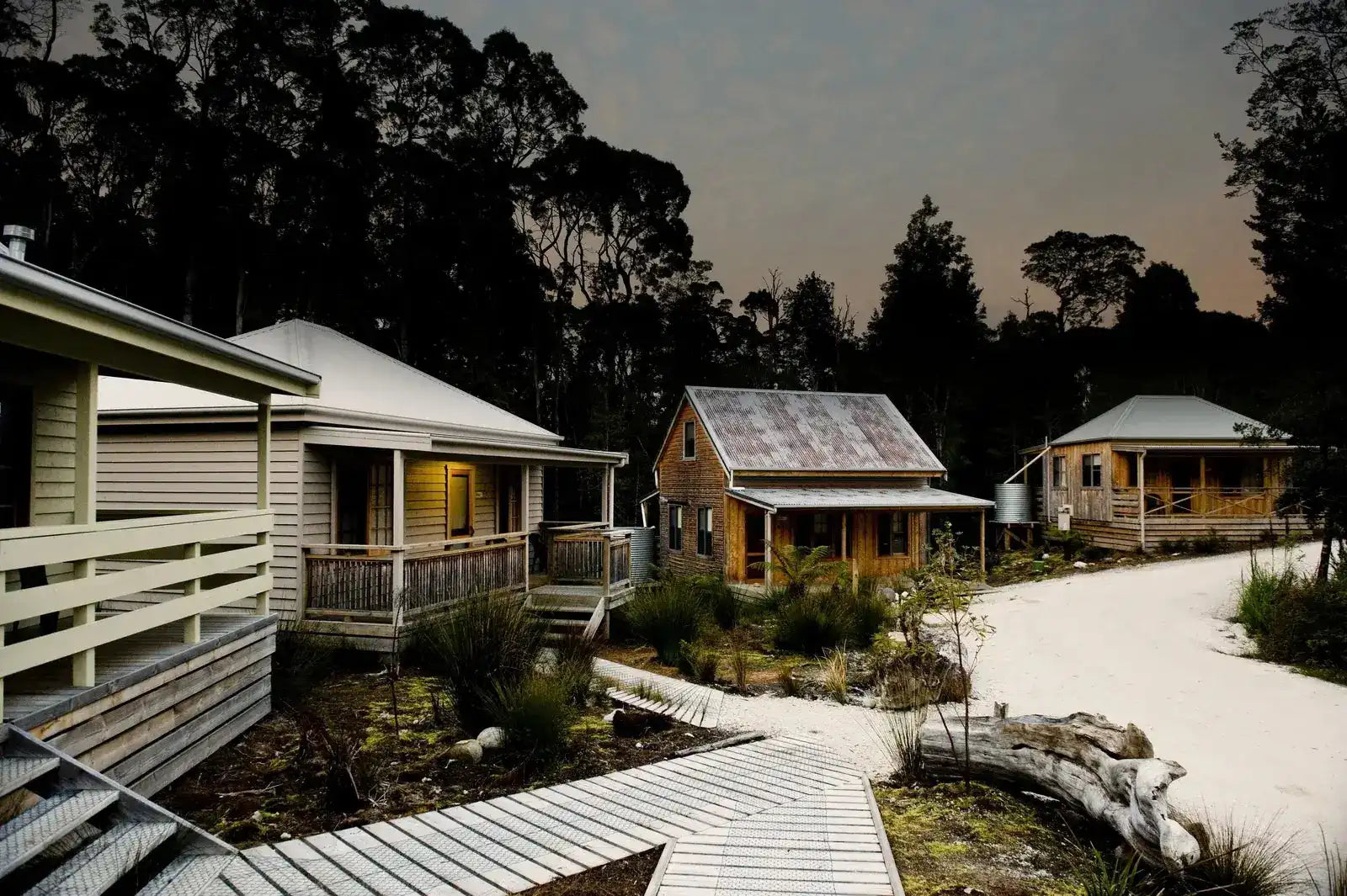 Three wooden cabins with a pathway leading to them, surrounded by trees.