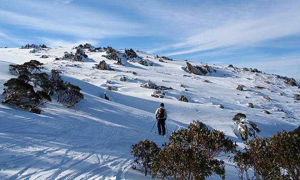 Person skiing on a snowy mountain with blue sky and scattered clouds