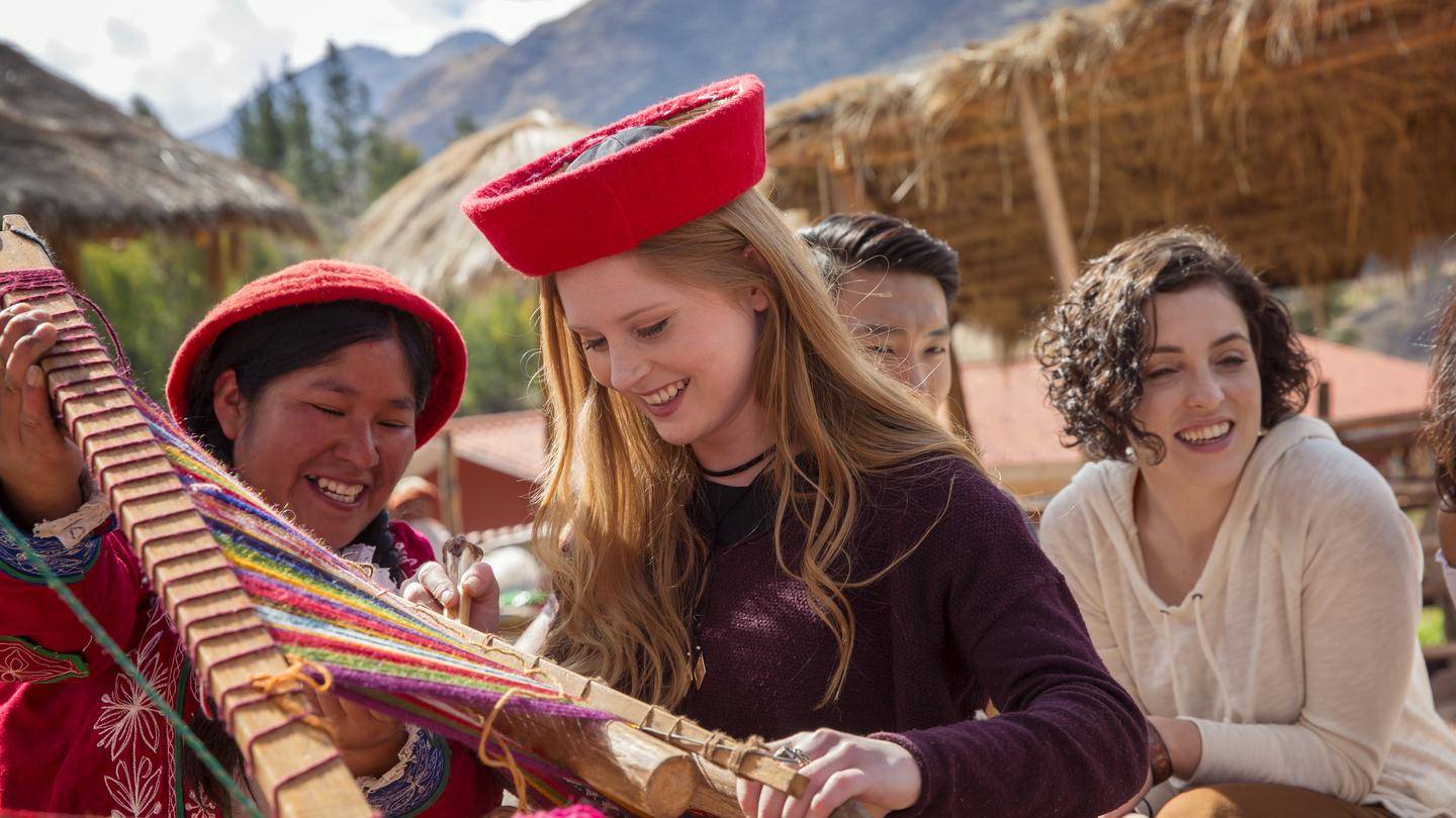 Tourists learning traditional weaving in Peru on the Quito to Rio South America tour. A cultural stop on the 15-65 day adventure.