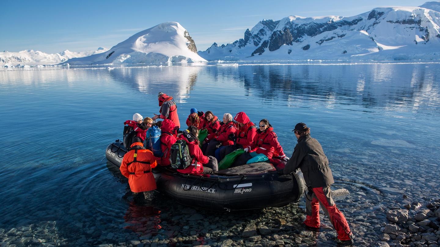 Travelers in red parkas board Zodiac boat for Antarctic shore landing on 11-day Antarctica Expedition Cruise - Edge of the Earth.
