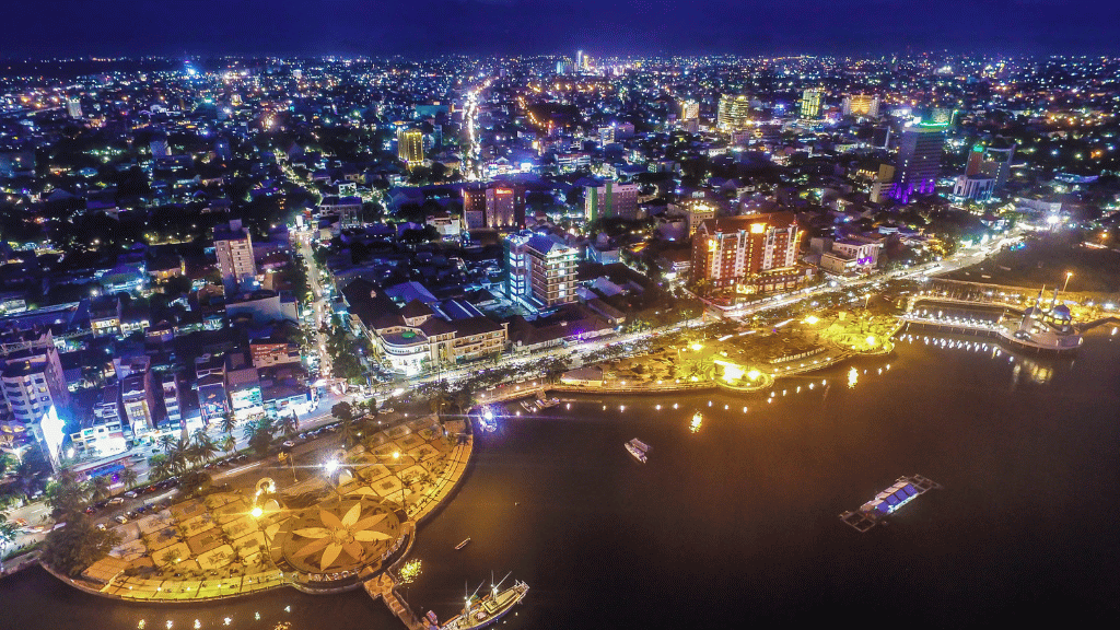 Night aerial view of Makassar city lights and waterfront, a vibrant urban stop on the Soul of Sulawesi - Tana Toraja Culture Tour.