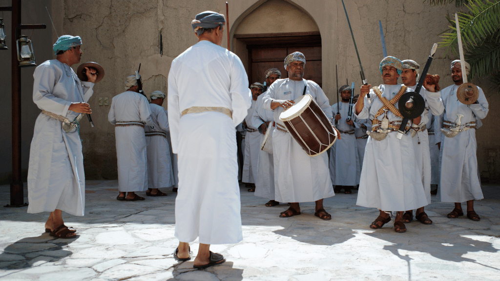 Omani men in traditional dress performing music and dance, a cultural experience on the Oman 8 Day Adventure - Desert Stars & Turtle Shores tour.