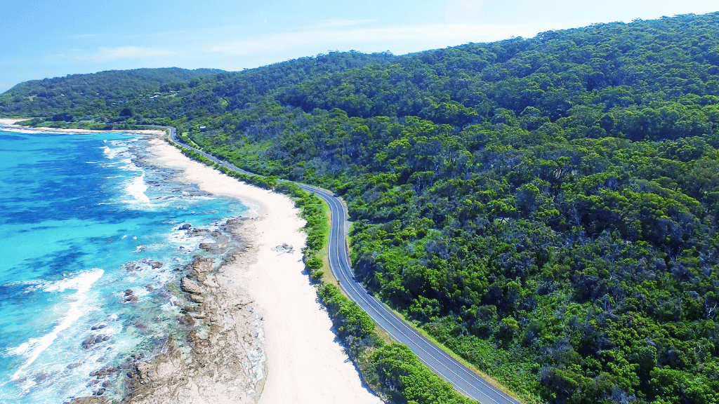 Aerial view of coastline road near turquoise waters and lush greenery, perfect for outdoor adventure tours.