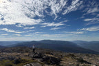Solo hiker admiring vast mountain landscape from Mt Bimberi summit on Blue Waterholes tour adventure.