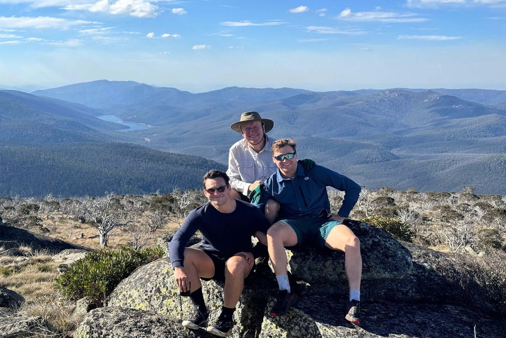 Three hikers resting on rocks with panoramic views of Namadgi National Park during Mt Bimberi tour adventure.