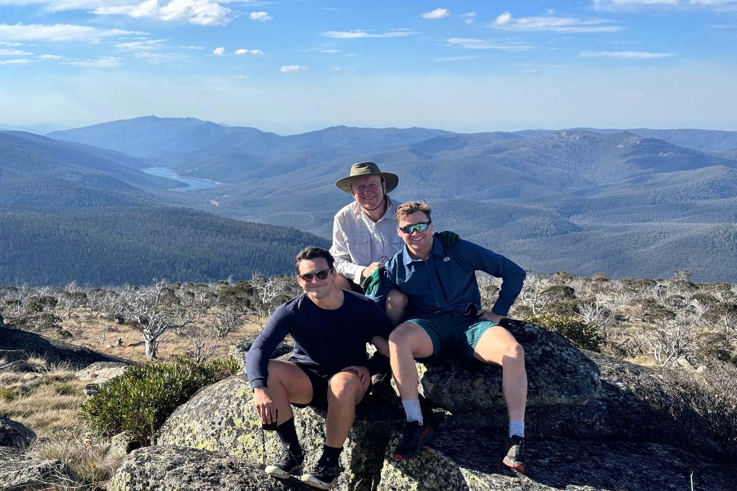 Three hikers resting on rocks with panoramic views of Namadgi National Park during Mt Bimberi tour adventure.