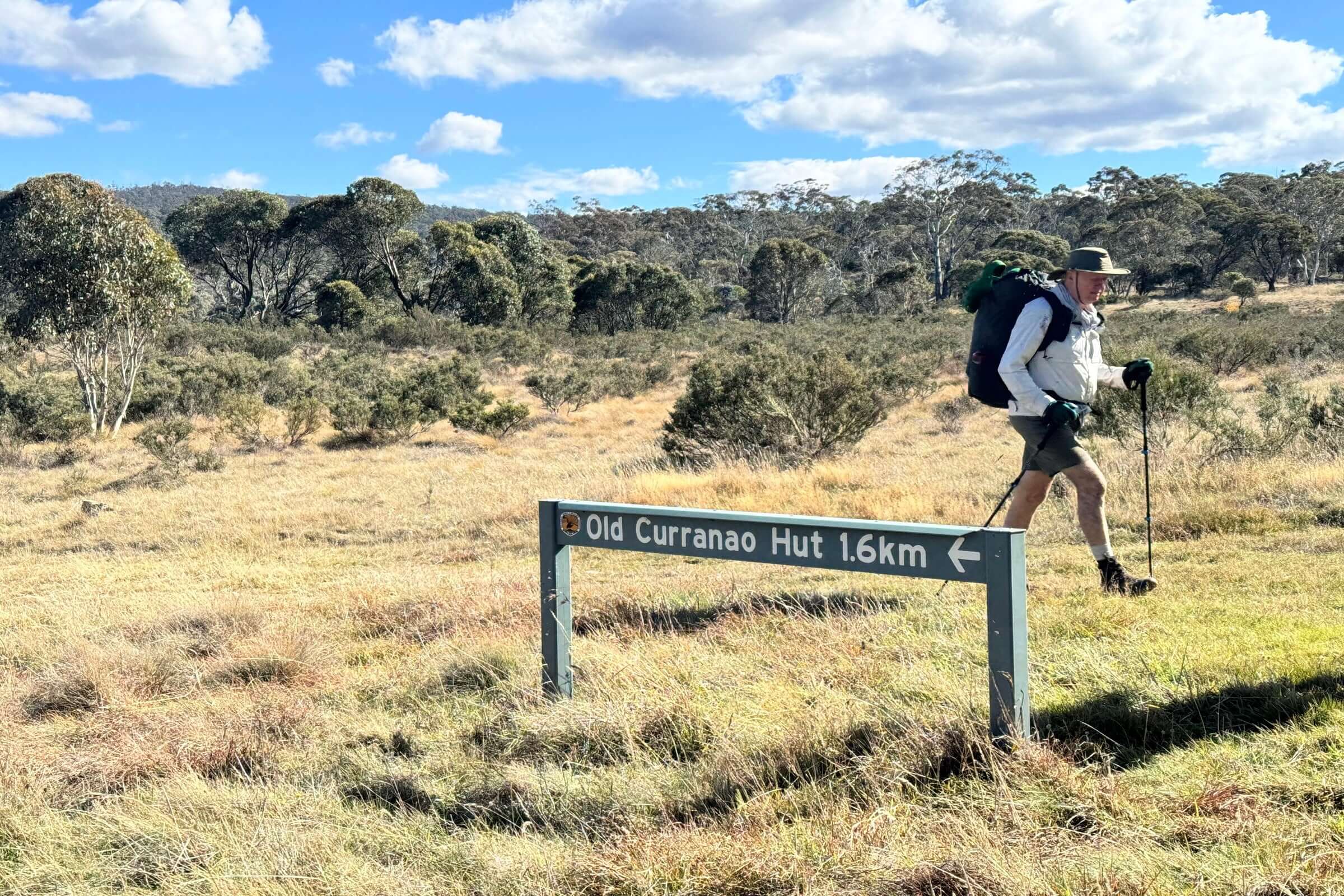 Hiker walking past Old Curranao Hut sign on scenic trail during Mt Bimberi & Blue Waterholes outdoor adventure.