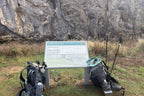 Coolaman Cave sign with hiking gear in front of limestone cliffs on Mt Bimberi & Blue Waterholes tour route.