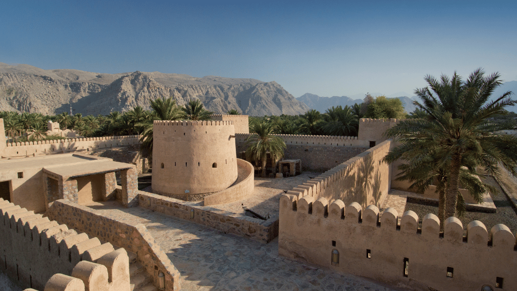 Historic Bahla Fort surrounded by palm trees and mountains, a UNESCO site on the Oman 8 Day Adventure - Desert Stars & Turtle Shores itinerary.