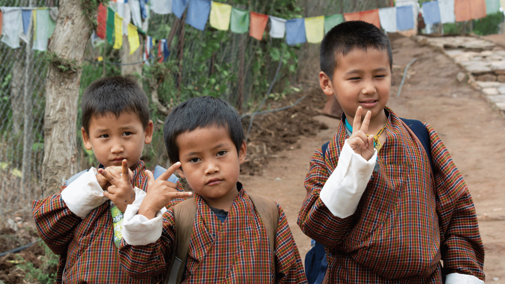 Bhutanese children in traditional dress smiling along the Trans Bhutan Trail, part of the cultural immersion experience.