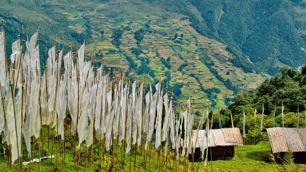 White prayer flags on a hillside overlooking rice terraces, a peaceful scene along the Trans Bhutan Trail.