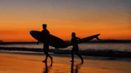 Surfers walk along beach at sunset, capturing coastal lifestyle on the Whitsundays Reef Tour from Brisbane to Cairns.