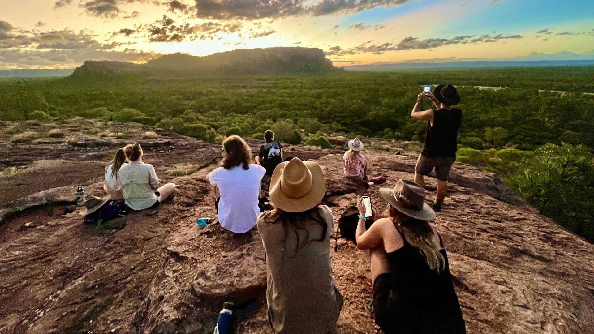 Group watching sunset from rocky lookout at Kakadu Litchfield Camping Adventure - 3-Day Tour. Scenic view over forest and cliffs.