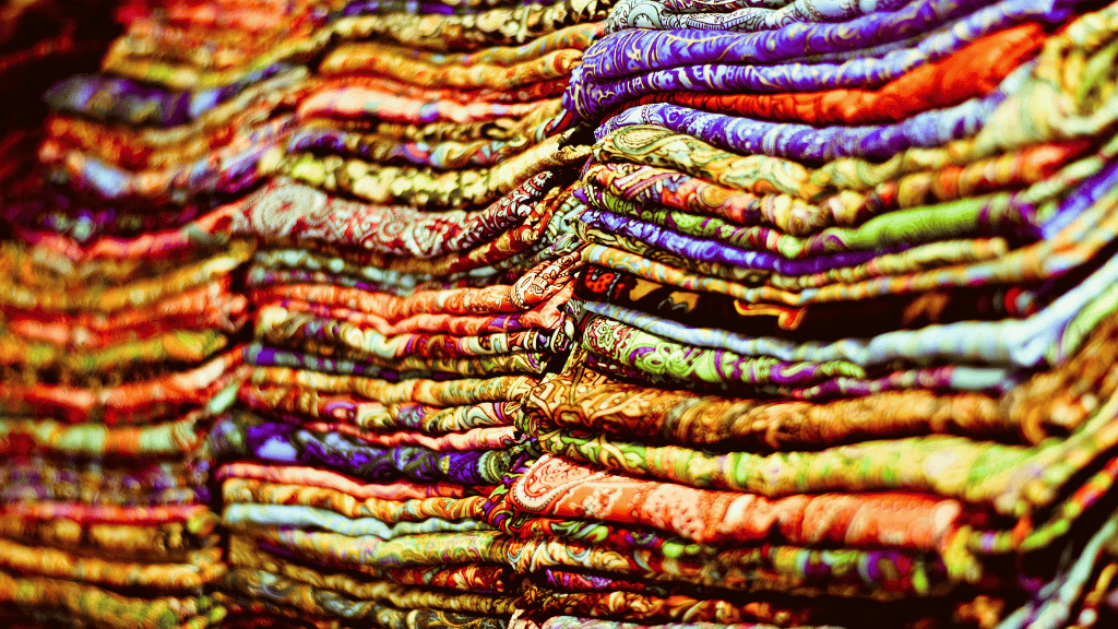 Stacks of colorful silk scarves in a Central Asian market, showcasing local crafts on the 14-23 Day Central Asia Silk Road Tour.