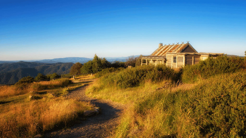 Abandoned rustic house on a hilltop with rolling mountains in the background during sunset.