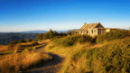 Abandoned rustic house on a hilltop with rolling mountains in the background during sunset.