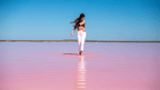 Woman walking through pink waters at Hutt Lagoon during West Coast Road Trip from Perth to Exmouth. Scenic outdoor activity in Western Australia.