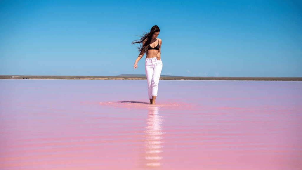 Woman walking through pink waters at Hutt Lagoon during West Coast Road Trip from Perth to Exmouth. Scenic outdoor activity in Western Australia.
