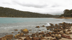 Coastal scene with rocky beach and turquoise water under a cloudy sky.