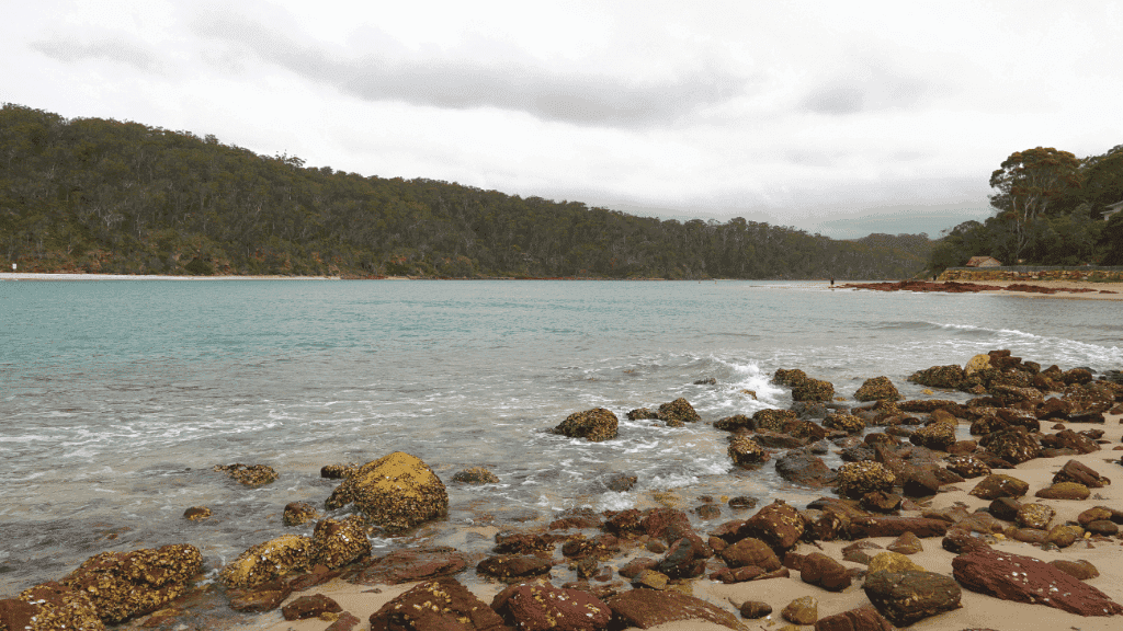 Coastal scene with rocky beach and turquoise water under a cloudy sky.
