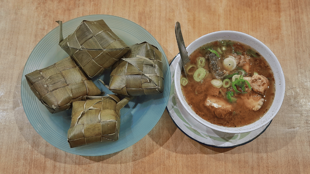 Traditional Sulawesi dish with ketupat rice and soup, part of the local cuisine on the Soul of Sulawesi - Tana Toraja Culture Tour.