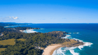 Aerial view of a coastal landscape with greenery, sandy beach, and blue ocean.