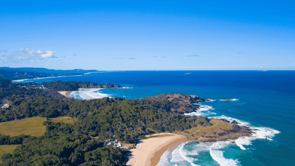 Aerial view of a coastal landscape with greenery, sandy beach, and blue ocean.