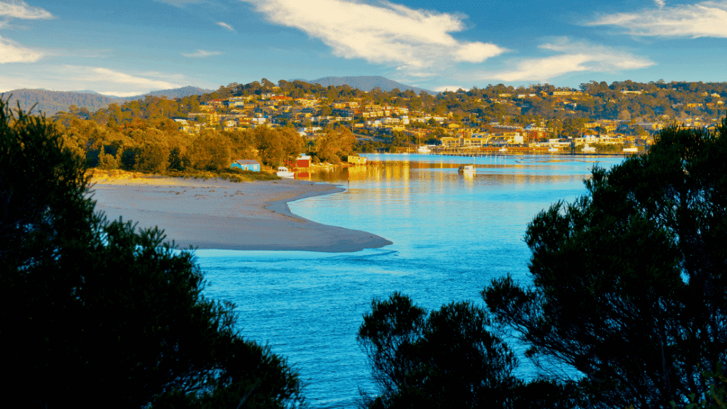 Scenic view of a beach with trees and houses on a hillside under a blue sky.