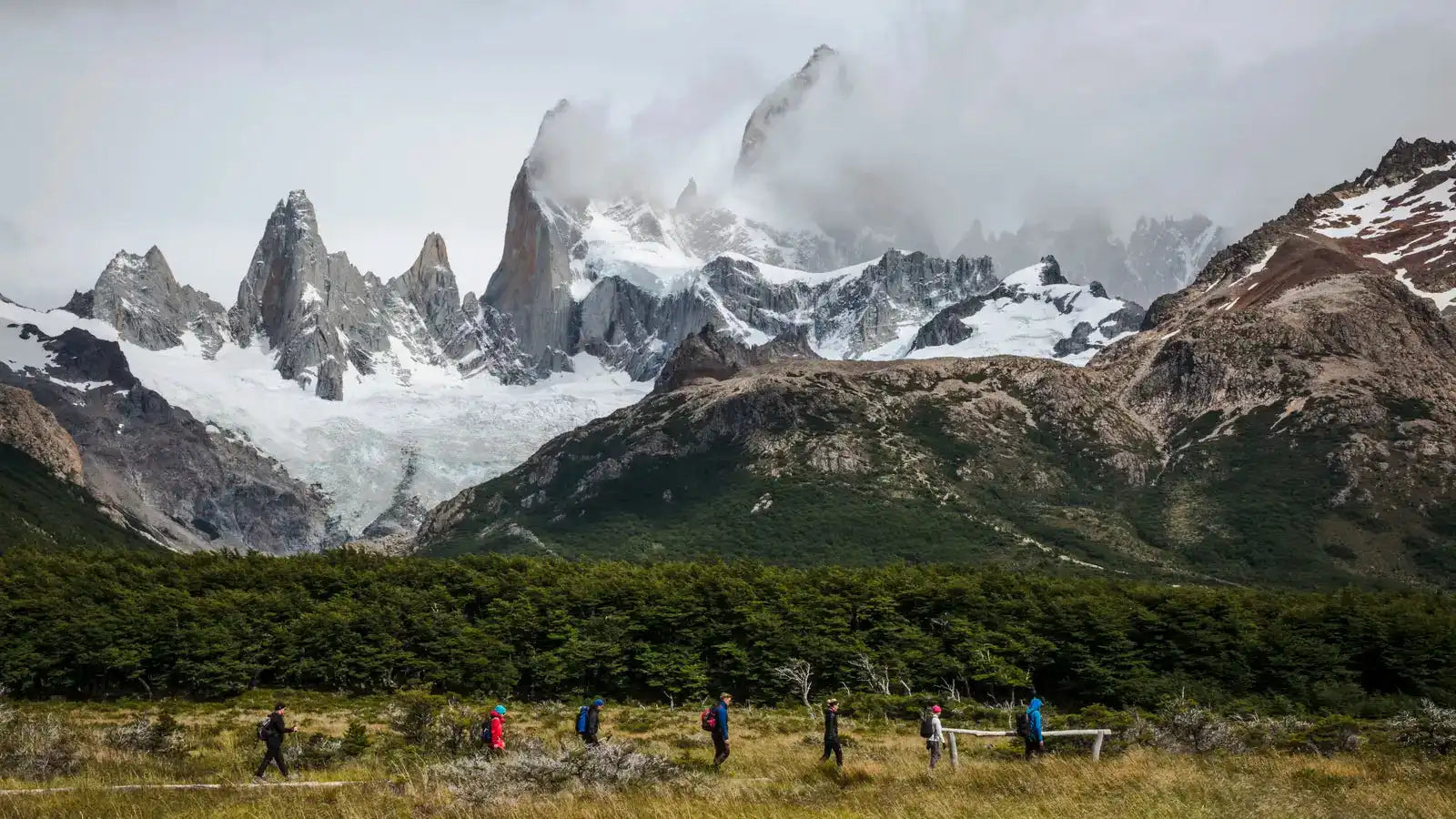 Group of hikers trekking below jagged peaks in Patagonia on the Blue Heart Adventure | 9 Days. Immersive hiking experience in glacier country.