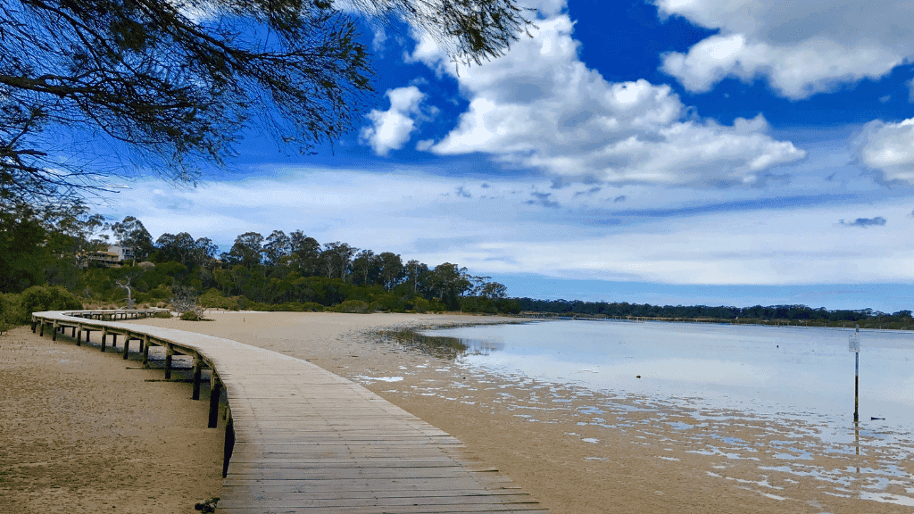 Wooden boardwalk leading to a beach with clear blue sky and clouds.