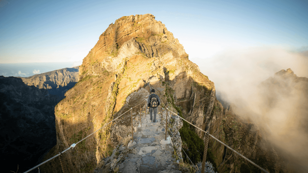 Hiker crossing a narrow mountain ridge trail in Madeira, a thrilling part of the 6-days hiking Madeira’s trails adventure.
