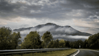 Misty mountain view alongside a winding road, surrounded by lush trees and a dramatic sky, perfect for outdoor adventures.