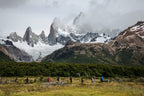 Group of people hiking in a grassy field with snow-capped mountains in the background