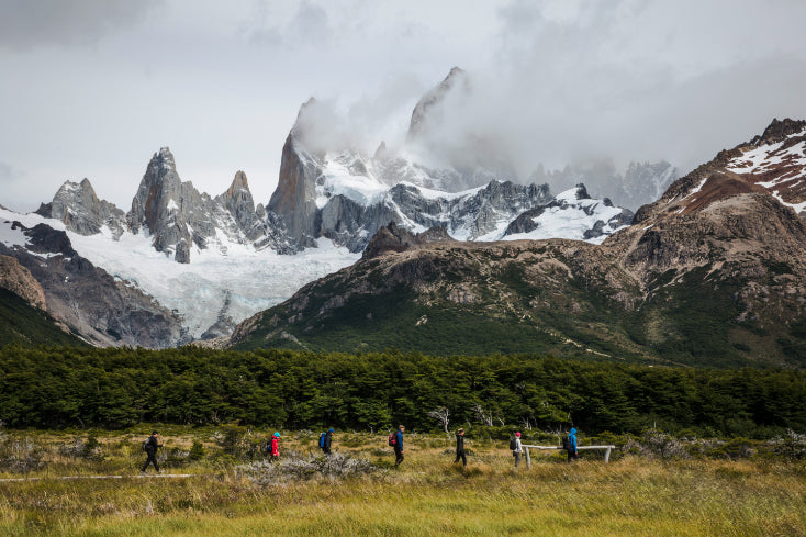Group of people hiking in a grassy field with snow-capped mountains in the background