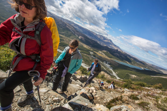 Hikers on a mountain trail with a scenic view of mountains and clouds.
