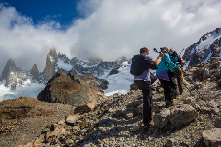 Hikers on a mountain peak with snow-capped peaks and clouds in the background
