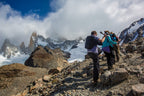 Hikers on a mountain peak with snow-capped peaks and clouds in the background