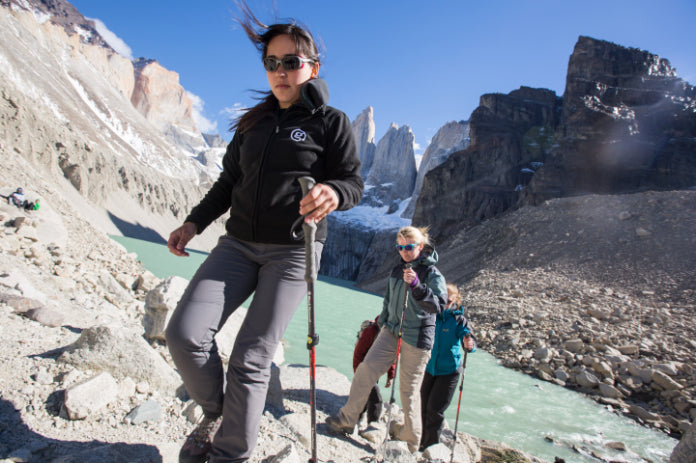 Two hikers on a mountain trail with a scenic view of a river and rocky cliffs.