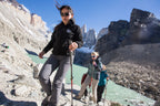 Two hikers on a mountain trail with a scenic view of a river and rocky cliffs.