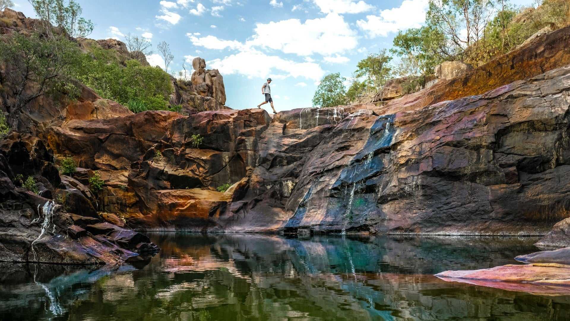 Traveler exploring rocky waterfall at Kakadu Litchfield Camping Adventure - 3-Day Tour. Natural plunge pool with cascading water and rugged terrain.