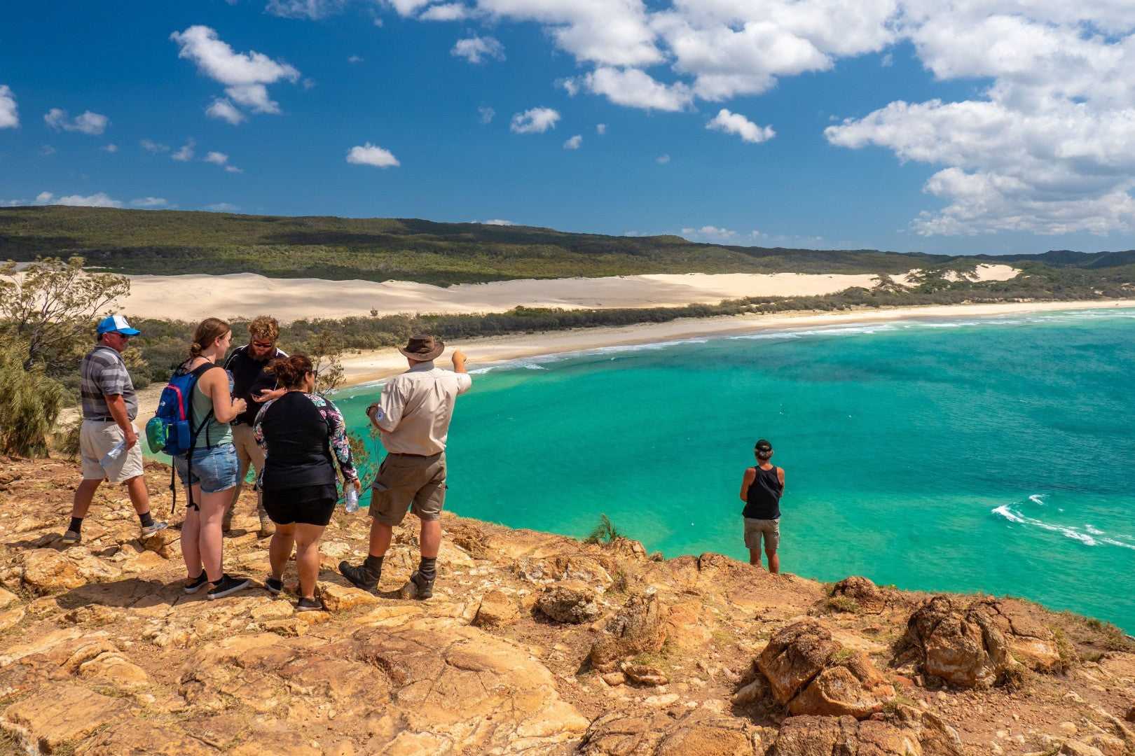 Group admires turquoise ocean from cliff on Fraser Island, part of the Whitsundays Reef Tour. Adventure stop on Brisbane to Cairns route.